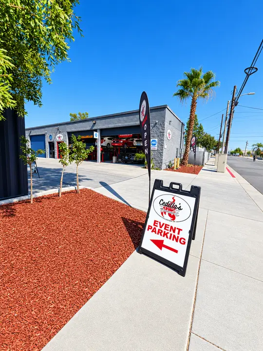 Sidewalk entrance to Cedillo's auto repair shop in Fullerton with A-frame parking sign and service bays in view
