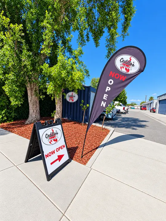 Cedillo's 'Now Open' feather flag and A-frame sign beside the shop driveway in Fullerton, California