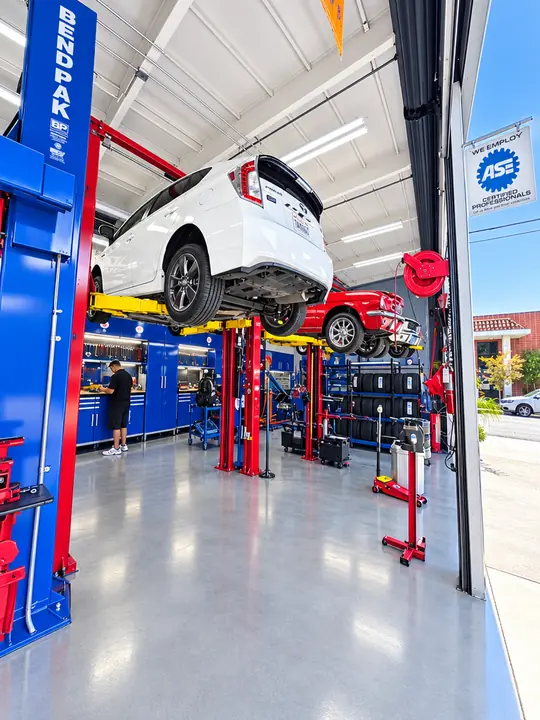 Open service bay with blue and red lifts and an SUV raised for repair at Cedillo's in Fullerton